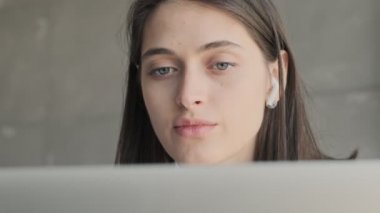 Evde genç ciddi bir iş kadını kablosuz kulaklıkla müzik dinlerken dizüstü bilgisayar kullanıyor.