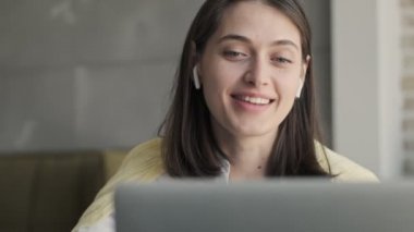 Evde genç bir iş kadını var. Laptop bilgisayarından kablosuz kulaklıkla konuşuyor.