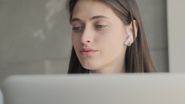 年轻而集中的女商人在家里一边用手提电脑一边用无线耳机听音乐 — 图库视频影像