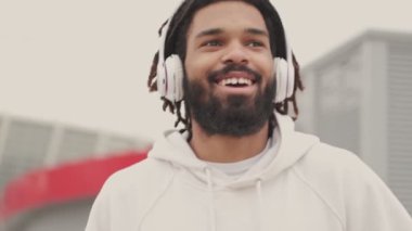Genç, iyimser, yakışıklı Afrikalı bir adam kulaklıkla müzik dinlerken dışarıda yürüyor.