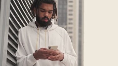 Genç konsantre olmuş ciddi Afrikalı adam dışarıda akıllı telefon kullanıyor.