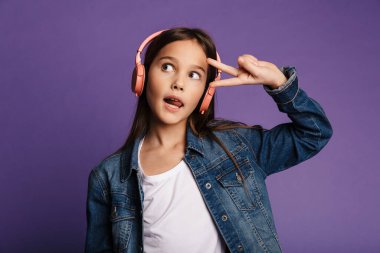 Güzel bir kızın barış işareti yaptığı ve mor arka planda izole edilmiş kablosuz kulaklık kullandığı bir fotoğraf.