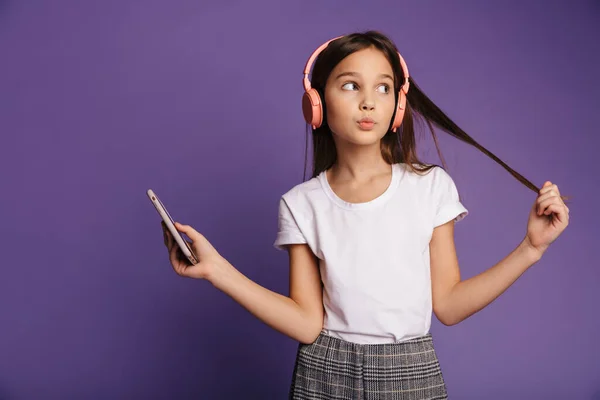 用无线耳机和紫色背景下隔离的手机进行思考的迷人女孩的照片 — 图库照片