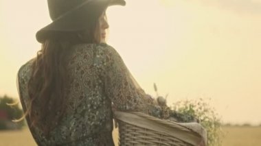 Buğday tarlasında piknikte elinde sepetle yürüyen şık şapkalı güzel bir kadın.