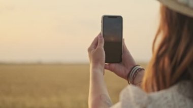 Buğday tarlasında akıllı telefondan fotoğraf çeken güzel bir kadın.