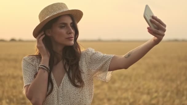 スマートフォンで自画撮りをしながら小麦畑でポーズをとる可愛い女性の笑顔 — ストック動画