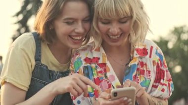 İki gülümseyen genç kız parkta yürürken akıllı telefondan fotoğraf izliyor.