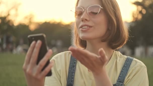 一位快乐的年轻女子在公园里散步的时候 正在用她的智能手机通过视频连接交谈 — 图库视频影像
