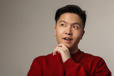 Gri arka planda yalnız bırakılmış, poz veren yakışıklı Asyalı bir adam.