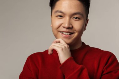 Gri arka planda izole edilmiş, gülümseyen ve kameraya bakan yakışıklı Asyalı adamın görüntüsü