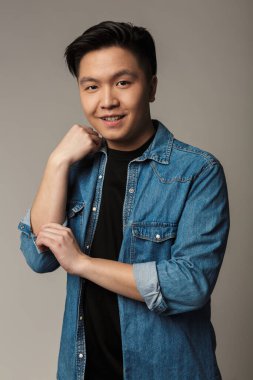 Gri arka planda izole edilmiş, gülümseyen ve kameraya bakan yakışıklı Asyalı bir adam.