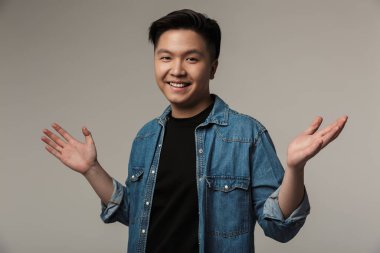 Gülümseyen neşeli Asyalı adam resmi. Gri arka planda izole edilmiş elleri kusuyor.