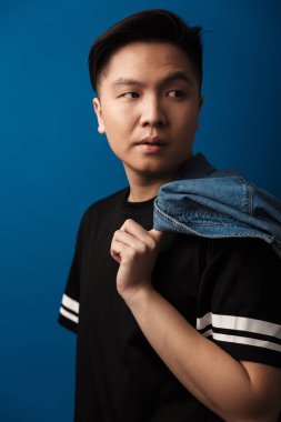 Kendine güvenen yakışıklı Asyalı adamın mavi arka planda izole edilmiş kot gömlekli hali.