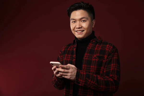 Image Cheerful Asian Man Smiling Using Mobile Phone Isolated Burgundy — Stock Photo, Image