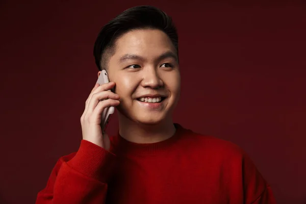 バーガンディを背景に孤立した携帯電話で笑顔と話す楽しいアジアの若者のイメージ — ストック写真