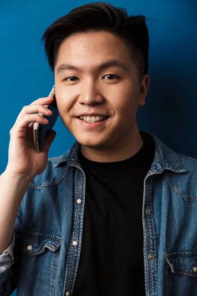 興奮したハンサムなアジアの男の笑顔と話しているのイメージ携帯電話で隔離された青の背景 — ストック写真