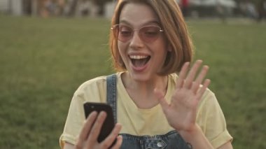 Mutlu genç bir kadın parkta yürürken akıllı telefonuyla video bağlantısı kuruyor.