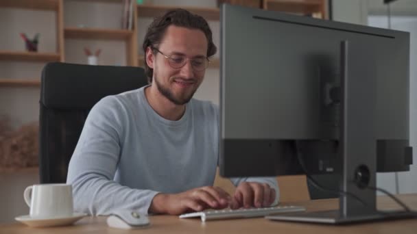Zadowolony Młody Biznesmen Pisze Coś Swoim Komputerze Siedząc Biurze — Wideo stockowe