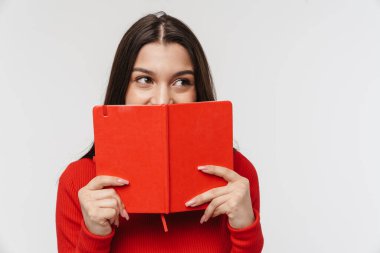Güzel, neşeli, esmer bir kadının portresi beyaz arka planda izole edilmiş, açık bir kitap tutuyor.
