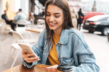 Gülümseyen güzel bir kadının sokak kafesinde otururken cep telefonu ve kredi kartı kullanması.