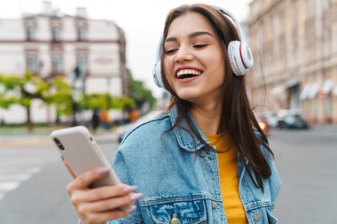 Akıllı telefon ve kablosuz kulaklıkla müzik dinleyen gülen güzel bir kadın görüntüsü.