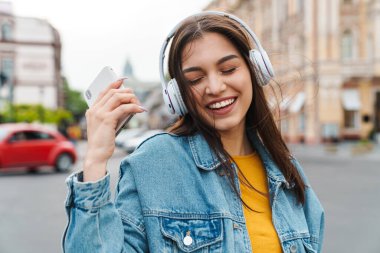 Akıllı telefon ve kablosuz kulaklıkla müzik dinleyen gülen güzel bir kadın görüntüsü.
