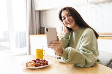 Modern mutfakta kahvaltı yaparken gülümseyen güzel bir kadının fotoğrafı.