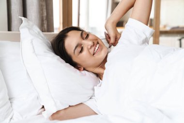 Basit tişörtlü güzel esmer bir kadının, uyuduktan sonra yatakta yatarken gülümsemesi ya da şekerleme yapması.