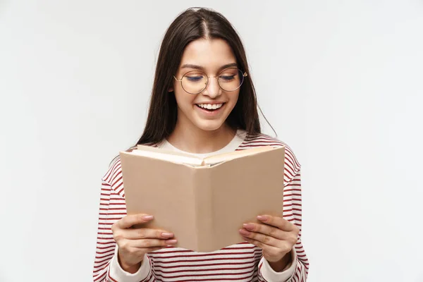 照片上 快乐的黑发女青年戴着眼镜 面带微笑 在白色背景下孤立地看书 — 图库照片