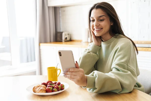 아름다운 여인이 주방에서 식사를 하면서 전화를 사용하여 — 스톡 사진