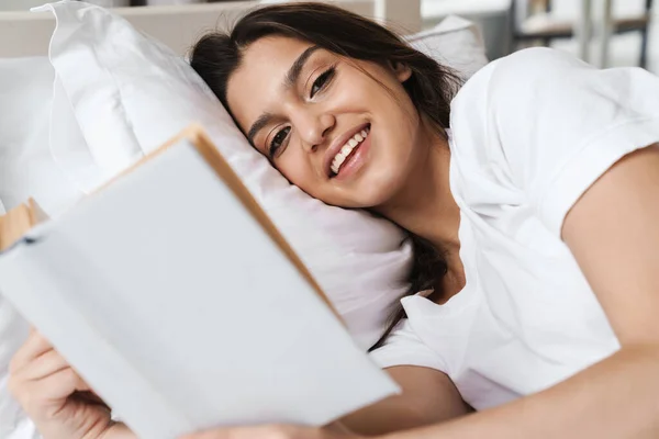Фото Сфокусированной Улыбающейся Красивой Женщины Читающей Книгу Лежащей Кровати После — стоковое фото