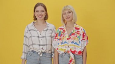 İki mutlu güzel kadın sarı arka planda hava öpücüğü yolluyor.