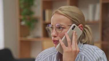Sarışın, güzel bir iş kadını ofiste otururken telefonla konuşuyor.