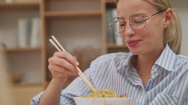 Ofiste dizüstü bilgisayarına bakarken yemek yiyen mutlu, sarışın bir iş kadınının yakın plan görüntüsü.
