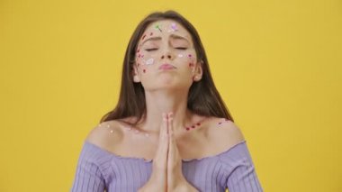 Yüzünde moda makyajı ve çıkartmaları olan çekici bir genç kız, sarı bir arka planda tek başına durmuş dua ederken bir şey istiyor.