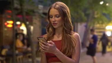 Genç ve güzel bir kadın yazın şehir parkında cep telefonunu kullanıyor.