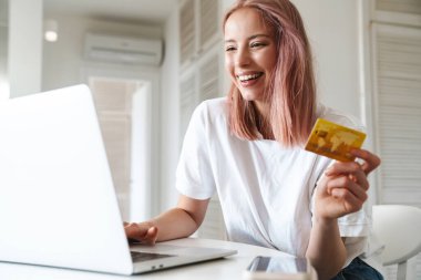 Bilgisayarla çalışan ve elinde kredi kartı olan neşeli bir kadının fotoğrafı.