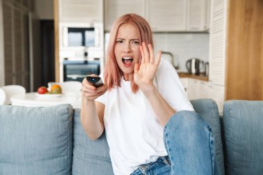 Güzel, korkmuş, çekici bir kadın oturma odasında bir kanepede dinleniyor.