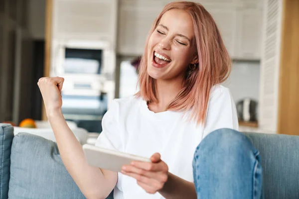 Image of delighted woman making winner gesture while playing video game on mobile phone at home