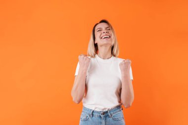 Mutlu genç bir kadının turuncu arka planda izole edilmiş gülüşü ve kazanan hareketi görüntüsü