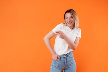 Gülen ve işaret eden neşeli güzel bir kadın görüntüsü turuncu arka planda izole edilmiş.