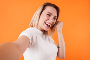Heyecanlı, tatlı bir kadının, turuncu arka planda izole edilmiş selfie çekerken yaptığı güzel bir jest.