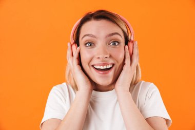 Portakal rengi arka planda izole edilmiş, gülümseyen ve kablosuz kulaklık kullanan neşeli genç bir kadın görüntüsü