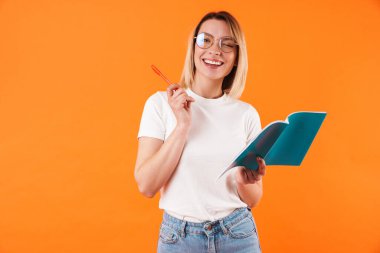 Portakal rengi arka planda izole edilmiş, günlük tutan neşeli, genç, sarışın bir kadının portresi.