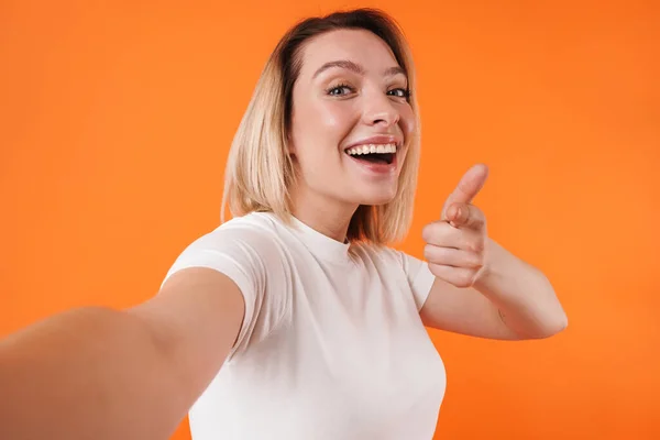 照片中快乐而和善的女人在拍摄橙色背景下的自拍照片时 用手指对着相机 — 图库照片