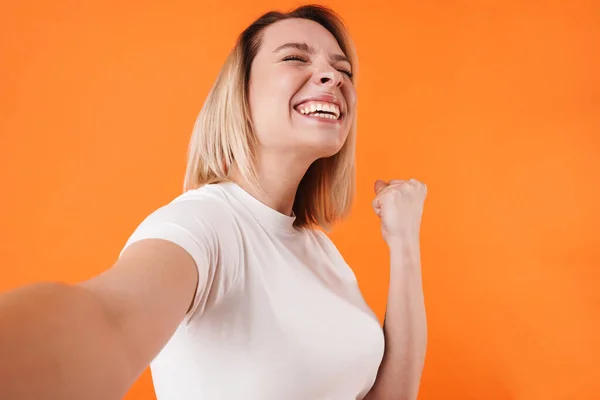 照片中兴奋而可爱的女人在拍摄橙色背景下的自拍照时做得奖手势 — 图库照片