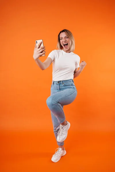Image Excited Woman Making Winner Gesture Using Cellphone Isolated Orange — Stock Photo, Image