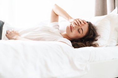 Basit tişörtlü güzel esmer bir kadının yataktan sonra yattığı ya da uyuduğu bir fotoğraf.