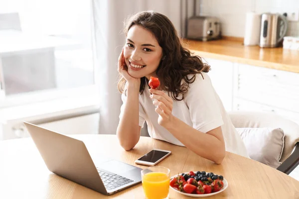 Φωτογραφία Της Χαρούμενης Όμορφης Γυναίκας Που Χρησιμοποιεί Laptop Και Τρώει — Φωτογραφία Αρχείου