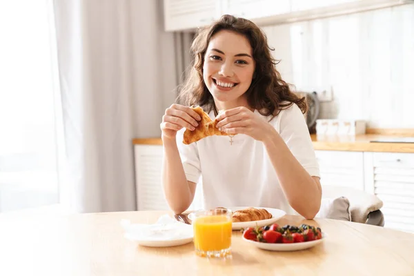 Foto Hermosa Mujer Alegre Sonriendo Comiendo Croissant Mientras Desayunaba Cocina — Foto de Stock